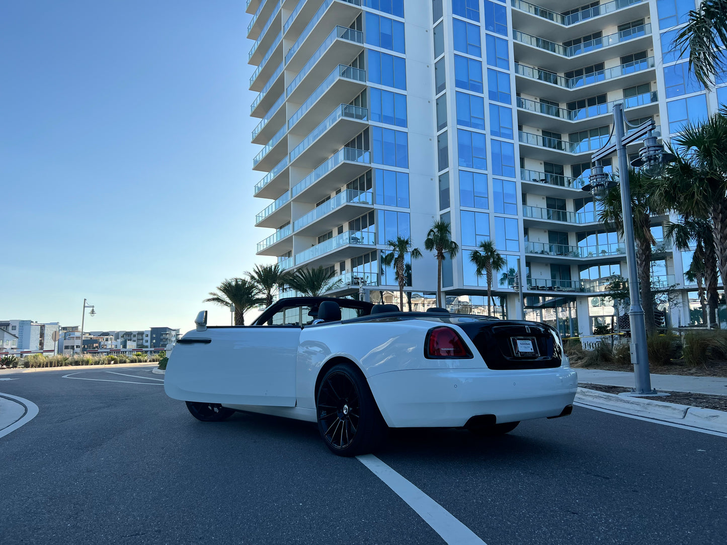Alt text: "Luxury white convertible Rolls-Royce parked by modern high-rise buildings, showcasing sleek design and sophisticated style perfect for upscale car enthusiasts and luxury rentals."