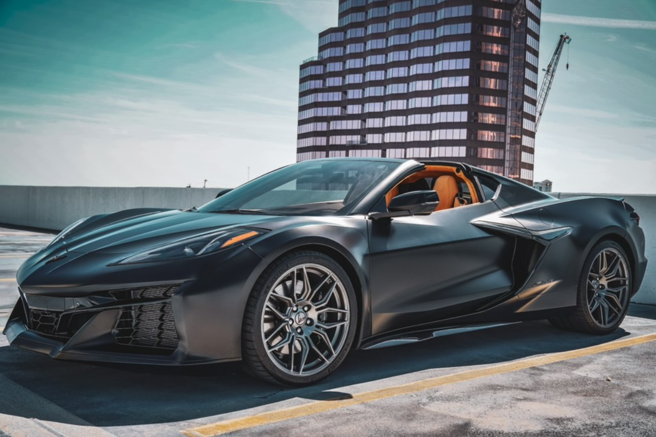 **Alt Text:** Sleek black Chevrolet Corvette C8 sports car parked on a rooftop, showcasing its striking design, custom matte finish, and luxurious orange leather interior, perfect for automotive enthusiasts seeking high performance and style.