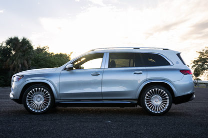 Alt text: "Side view of a stylish silver luxury SUV parked on a scenic road, showcasing its sleek design and high-performance wheels, perfect for families and adventure seekers."