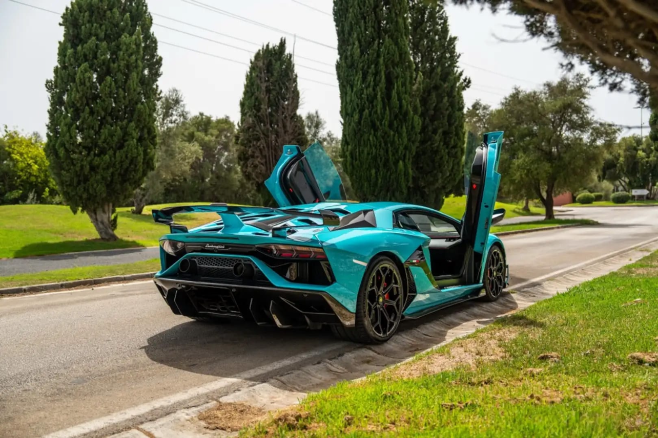 Turquoise sports car with open doors on a road with trees in the background