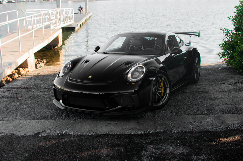 Black sports car parked near a waterfront with buildings in the background