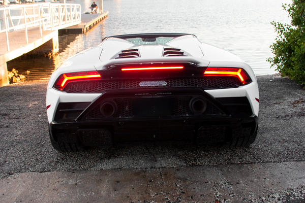 Back view of a white sports car with red taillights on a road near water and buildings.