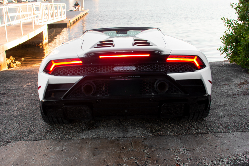 Back view of a white sports car with red taillights on a road near water and buildings.