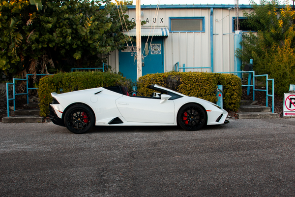 White sports car parked on a street with a building and trees in the background