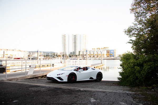 White sports car parked on a gravel area with buildings and trees in the background