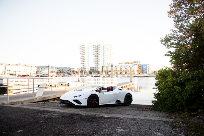 White sports car parked on a gravel area with buildings and trees in the background