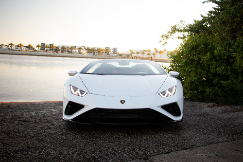 White sports car parked by a waterfront with trees in the background