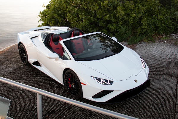White sports car parked by a waterfront with trees in the background