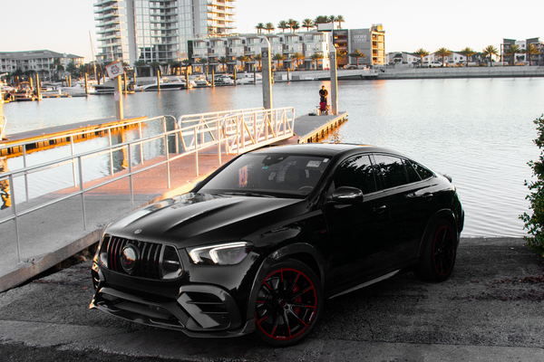 Black car parked by a waterfront with buildings in the background