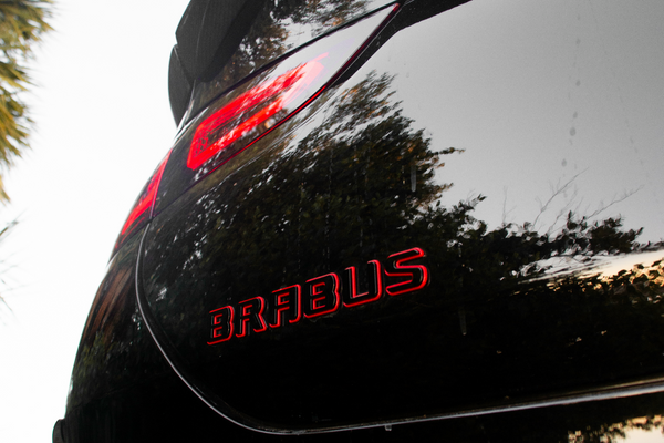 Back of a black car with 'AMG' logo on a blurred outdoor background