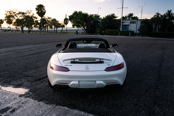 White convertible car on a road with trees and sunset in the background