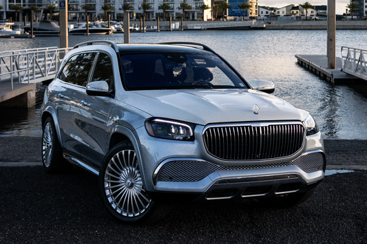 Luxury car parked by a waterfront with buildings in the background