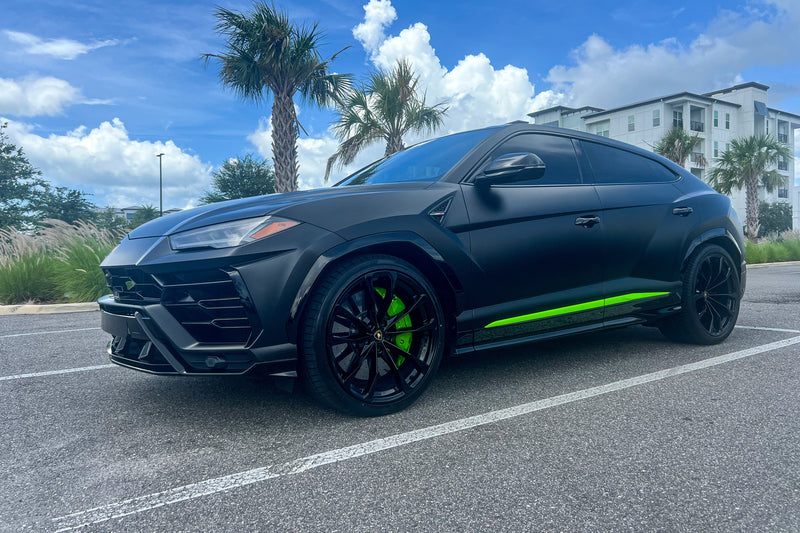 Black luxury SUV with green accent on a road with palm trees and buildings in the background