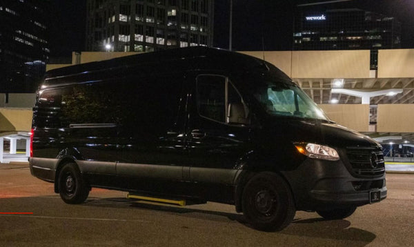 Black van parked on a street at night with city buildings in the background