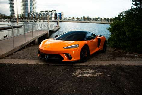 Orange sports car parked by a waterfront with buildings in the background