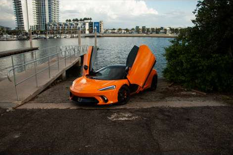 Orange sports car parked by a waterfront with buildings in the background