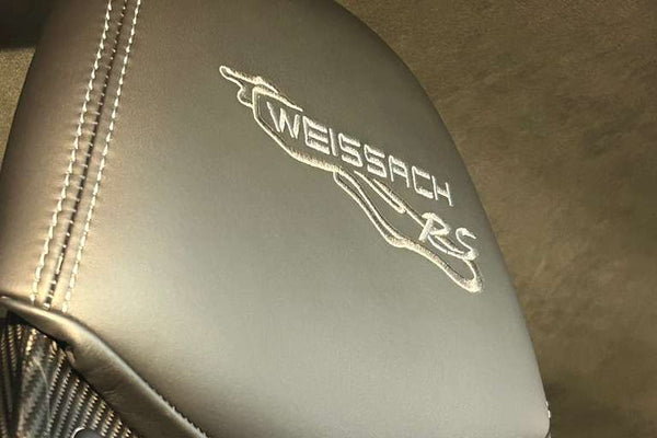 Close-up of a car seat with 'Weissach RS' branding on a carbon fiber background