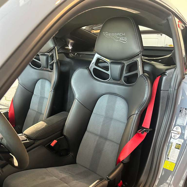 Car interior with black leather seats and red seat belts.